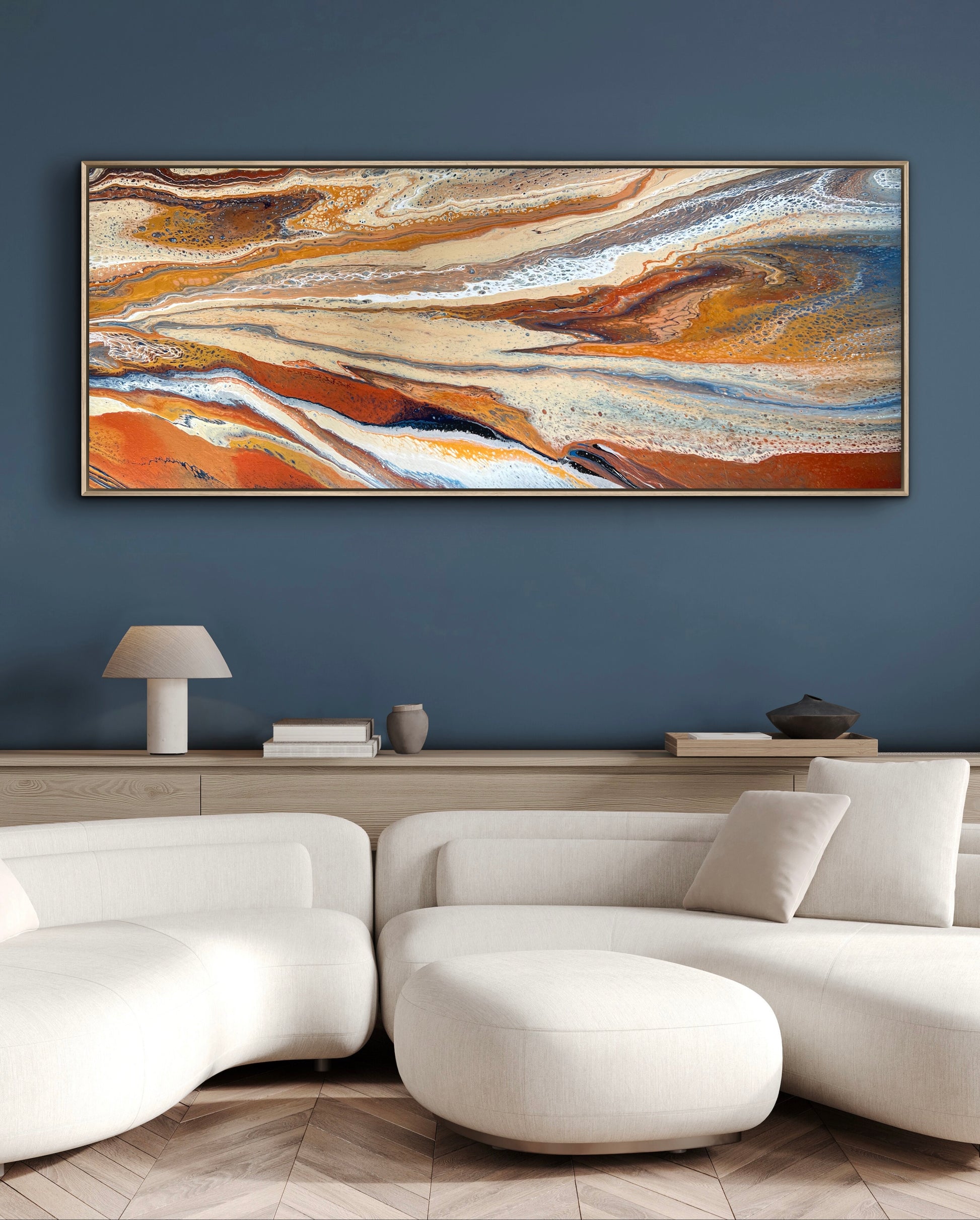 Desert Drift horizontal abstract painting displayed above a white sectional sofa against a deep blue wall