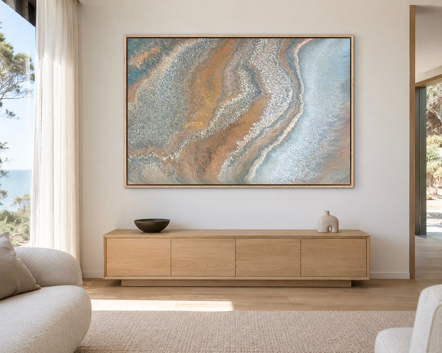 Weathered Tides blue and ochre coastal abstract painting displayed above a light timber console in a sunlit coastal living room

