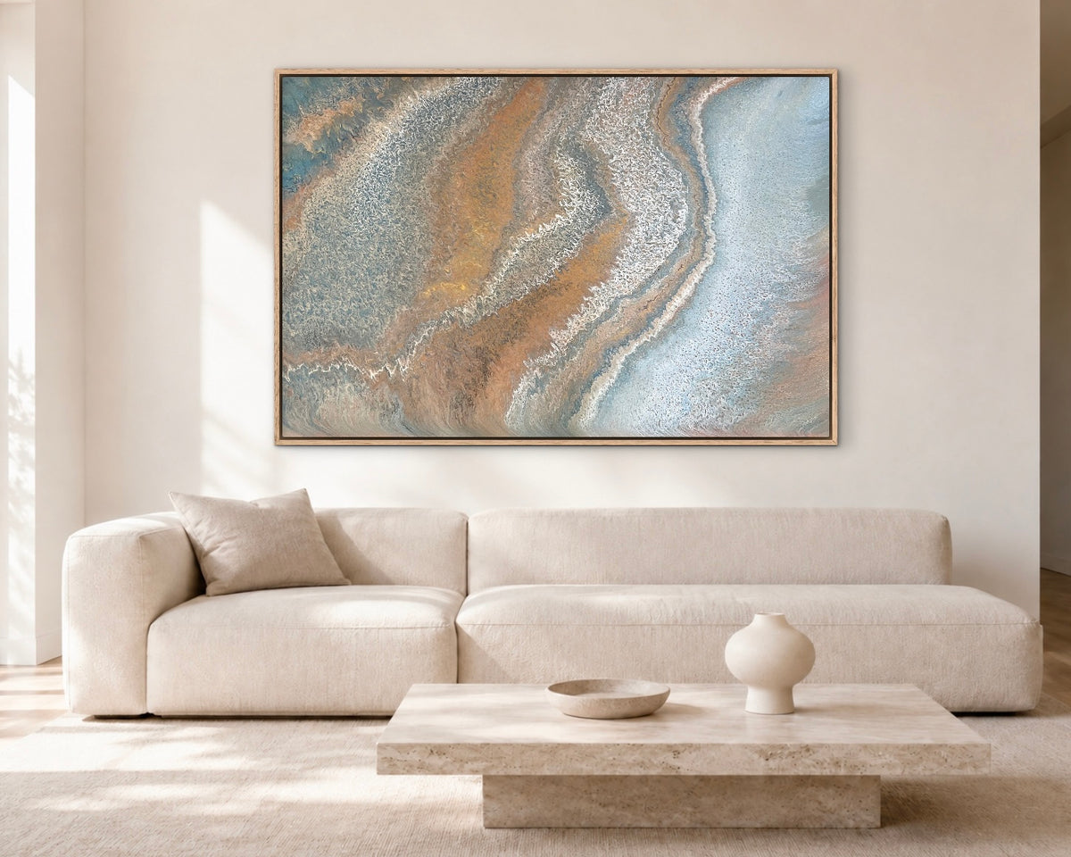 Weathered Tides blue, ochre and bronze coastal abstract painting displayed above a cream sofa in a bright modern living room
