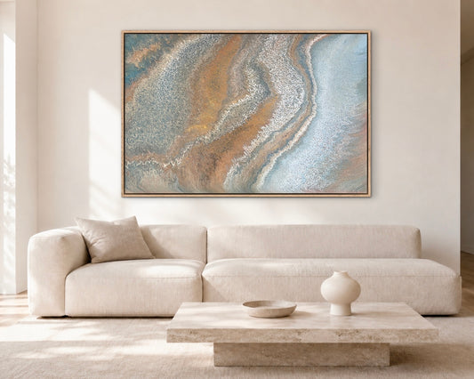 Weathered Tides blue, ochre and bronze coastal abstract painting displayed above a cream sofa in a bright modern living room
